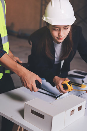 Construction manager and engineer dressed in orange work vests and hard helmets explore construction documentation on the building site near the steel framesの写真素材