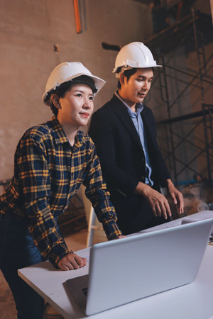 Construction manager and engineer dressed in orange work vests and hard helmets explore construction documentation on the building site near the steel framesの写真素材
