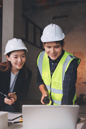 Construction manager and engineer dressed in orange work vests and hard helmets explore construction documentation on the building site near the steel framesの写真素材