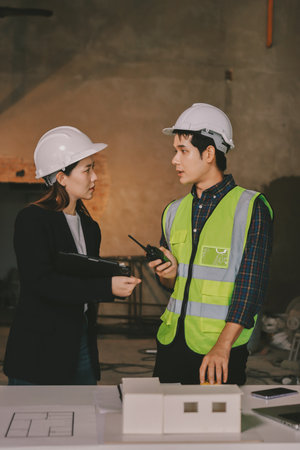 Construction manager and engineer dressed in orange work vests and hard helmets explore construction documentation on the building site near the steel framesの写真素材