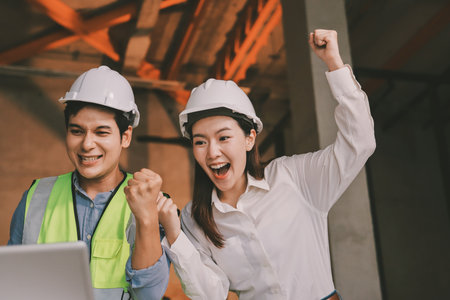 Construction manager and engineer dressed in orange work vests and hard helmets explore construction documentation on the building site near the steel framesの写真素材