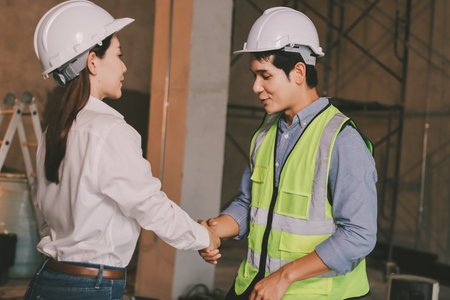 Construction manager and engineer dressed in orange work vests and hard helmets explore construction...