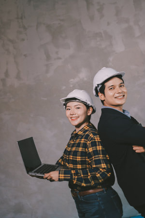 Construction manager and engineer dressed in orange work vests and hard helmets explore construction documentation on the building site near the steel framesの写真素材