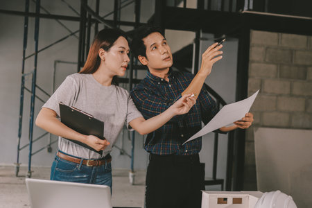 Construction manager and engineer dressed in orange work vests and hard helmets explore construction documentation on the building site near the steel framesの写真素材