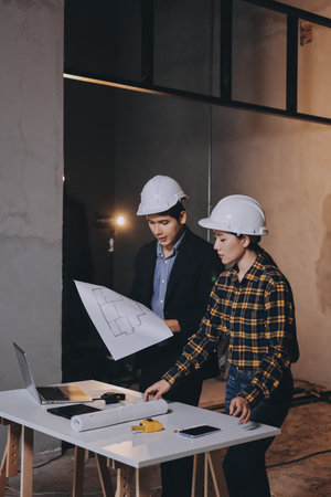 Construction manager and engineer dressed in orange work vests and hard helmets explore construction...