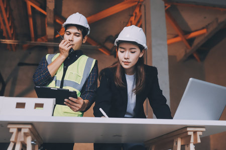 Construction manager and engineer dressed in orange work vests and hard helmets explore construction...