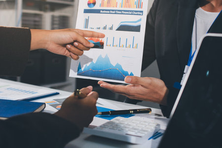 Focused young businessman signing agreement with skilled lawyer in eyeglasses. Concentrated financial advisor showing place for signature on paper contract document to male client at meeting in officeの写真素材