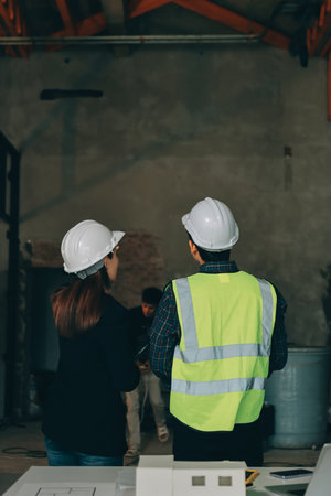 Construction manager and engineer dressed in orange work vests and hard helmets explore construction...