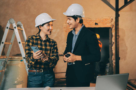 Construction manager and engineer dressed in orange work vests and hard helmets explore construction documentation on the building site near the steel framesの写真素材