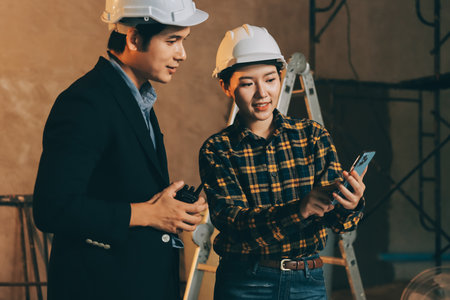 Construction manager and engineer dressed in orange work vests and hard helmets explore construction...