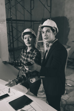 Construction manager and engineer dressed in orange work vests and hard helmets explore construction...