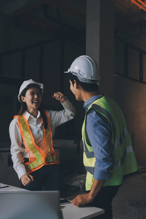Construction manager and engineer dressed in orange work vests and hard helmets explore construction...