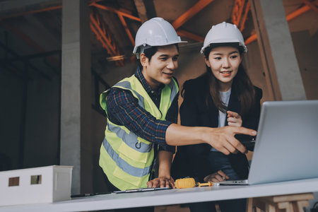 Construction manager and engineer dressed in orange work vests and hard helmets explore construction...
