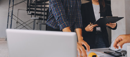 Construction manager and engineer dressed in orange work vests and hard helmets explore construction documentation on the building site near the steel framesの写真素材
