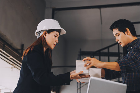 Construction manager and engineer dressed in orange work vests and hard helmets explore construction documentation on the building site near the steel framesの写真素材