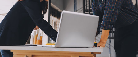 Construction manager and engineer dressed in orange work vests and hard helmets explore construction documentation on the building site near the steel framesの写真素材