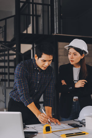 Construction manager and engineer dressed in orange work vests and hard helmets explore construction documentation on the building site near the steel framesの写真素材