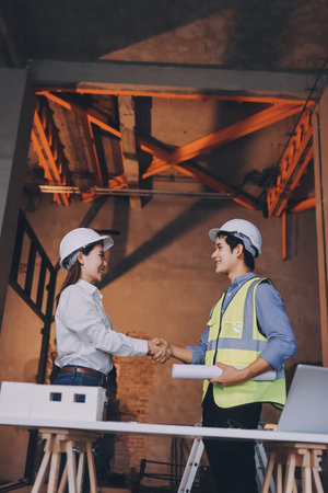 Construction manager and engineer dressed in orange work vests and hard helmets explore construction documentation on the building site near the steel framesの写真素材