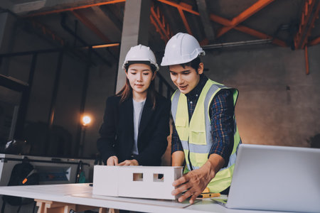 Construction manager and engineer dressed in orange work vests and hard helmets explore construction documentation on the building site near the steel framesの写真素材