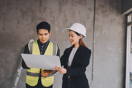Construction manager and engineer dressed in orange work vests and hard helmets explore construction documentation on the building site near the steel framesの写真素材