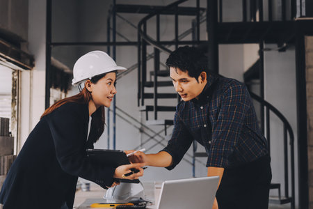 Construction manager and engineer dressed in orange work vests and hard helmets explore construction documentation on the building site near the steel framesの写真素材