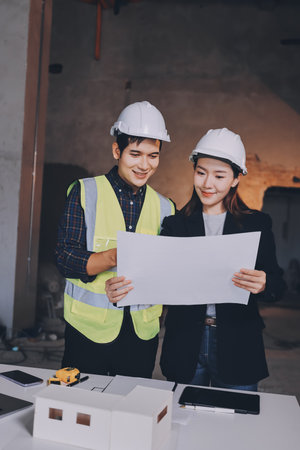 Construction manager and engineer dressed in orange work vests and hard helmets explore construction documentation on the building site near the steel framesの写真素材