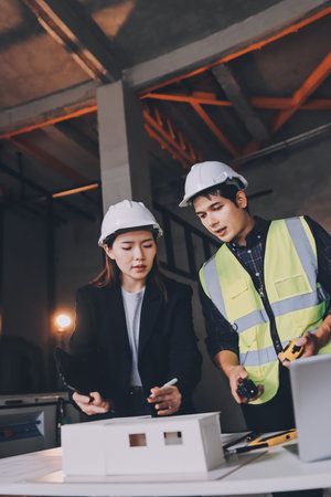 Construction manager and engineer dressed in orange work vests and hard helmets explore construction documentation on the building site near the steel framesの写真素材