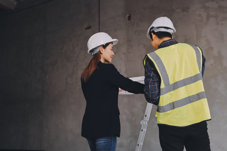Construction manager and engineer dressed in orange work vests and hard helmets explore construction documentation on the building site near the steel framesの写真素材