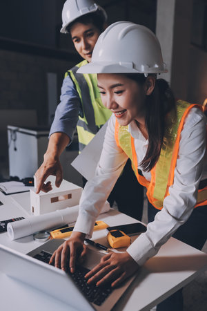 Construction manager and engineer dressed in orange work vests and hard helmets explore construction documentation on the building site near the steel framesの写真素材