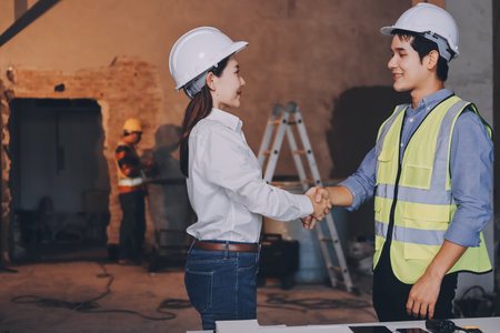Construction manager and engineer dressed in orange work vests and hard helmets explore construction...