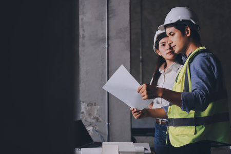 Construction manager and engineer dressed in orange work vests and hard helmets explore construction documentation on the building site near the steel framesの写真素材