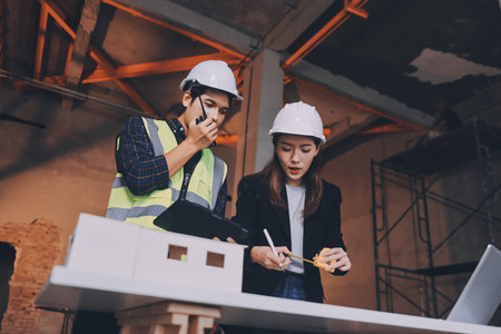 Construction manager and engineer dressed in orange work vests and hard helmets explore construction documentation on the building site near the steel framesの写真素材