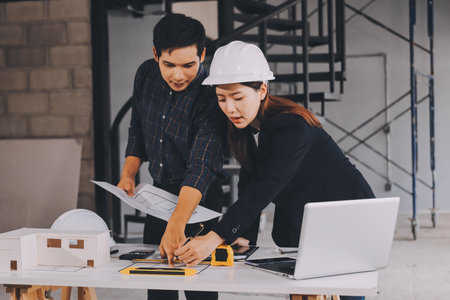 Construction manager and engineer dressed in orange work vests and hard helmets explore construction documentation on the building site near the steel framesの写真素材