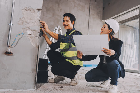 Construction manager and engineer dressed in orange work vests and hard helmets explore construction documentation on the building site near the steel framesの写真素材