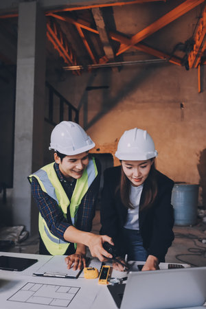 Construction manager and engineer dressed in orange work vests and hard helmets explore construction documentation on the building site near the steel framesの写真素材