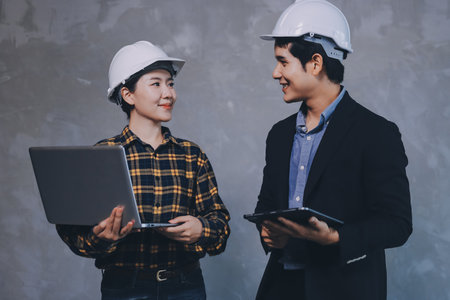 Construction manager and engineer dressed in orange work vests and hard helmets explore construction documentation on the building site near the steel framesの写真素材