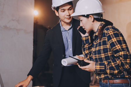 Construction manager and engineer dressed in orange work vests and hard helmets explore construction documentation on the building site near the steel framesの写真素材