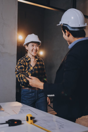 Construction manager and engineer dressed in orange work vests and hard helmets explore construction documentation on the building site near the steel framesの写真素材