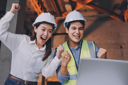 Construction manager and engineer dressed in orange work vests and hard helmets explore construction documentation on the building site near the steel framesの写真素材