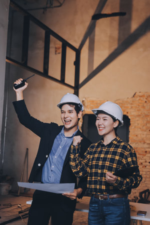 Construction manager and engineer dressed in orange work vests and hard helmets explore construction documentation on the building site near the steel framesの写真素材