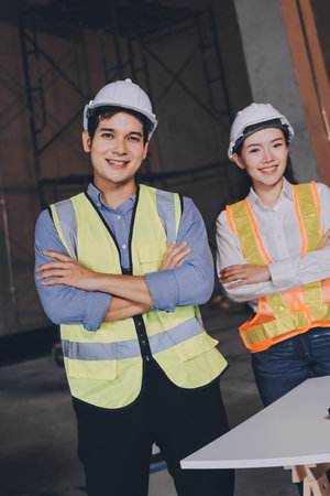 Construction manager and engineer dressed in orange work vests and hard helmets on the building site near the steel framesの写真素材