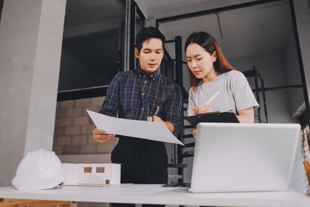 Construction manager and engineer dressed in orange work vests and hard helmets explore construction documentation on the building site near the steel framesの写真素材