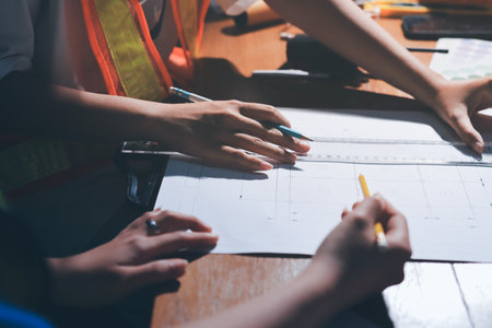 Closeup of team of industrial engineers meeting analyze machinery blueprints consult project on table in manufacturing factory. Working in manufacturing plant or production plant.の写真素材