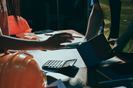 Closeup of team of industrial engineers meeting analyze machinery blueprints consult project on table in manufacturing factory. Working in manufacturing plant or production plant.の写真素材