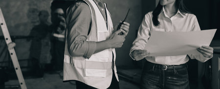 Construction manager and engineer dressed in work vests and hard helmets explore construction documentation on the building site near the steel framesの写真素材