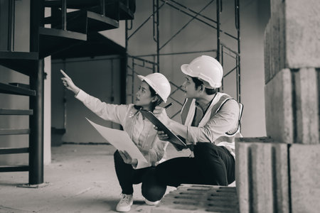 Construction manager and engineer dressed in orange work vests and hard helmets explore construction documentation on the building site near the steel framesの写真素材