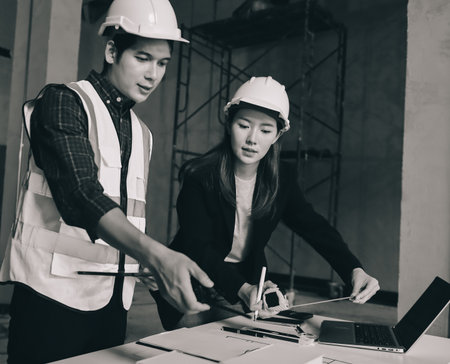 Construction manager and engineer dressed in work vests and hard helmets explore construction documentation on the building site near the steel framesの写真素材