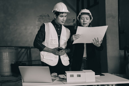 Construction manager and engineer dressed in white work vests and hard helmets explore construction documentation on the building site near the steel framesの写真素材