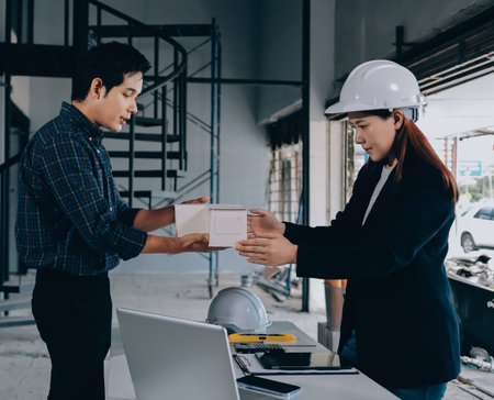 Construction manager and engineer dressed in orange work vests and hard helmets explore construction documentation on the building site near the steel framesの写真素材