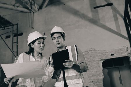 Construction manager and engineer dressed in orange work vests and hard helmets explore construction documentation on the building site near the steel framesの写真素材